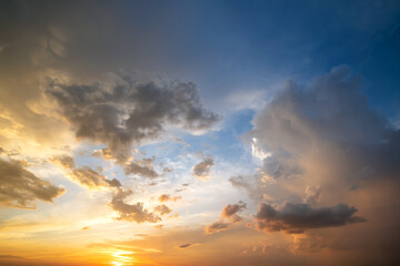 Naklejka na ściany i meble Dramatic sunset sky landscape with puffy clouds lit by orange setting sun and blue heavens