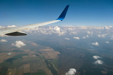 View of jet airplane wing from inside flying over white puffy clouds in blue sky. Travel and air transportation concept