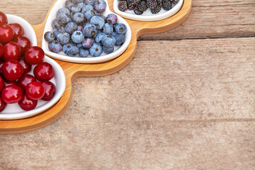 Portion wooden dish on light wooden background top view. Wooden partitioned dish divided into equal 3 section with berries.Compartmentals dish for food, dessert, fruit, berries and vegetable.
