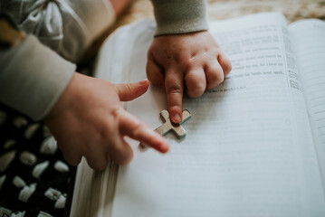 Child's hand playing with metal cross on open Bible