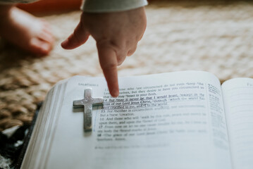 Naklejka premium Child's hand pointing to Bible verse with metal cross on page