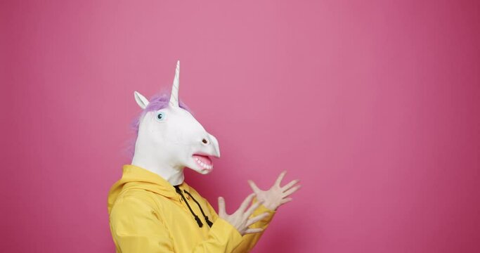 Funny in yellow clothes with Unicorn Mask shocked on isolated Pink Background, Having Fun, Party Halloween. Slow Motion. April 1, Fool's Day. Masquarade idea. Crazy emotion and gestured with his hands