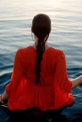 back of a woman in a wet red dress with long hair in blue water
