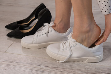 Naklejka premium Close-up business woman takes off her shoes puts on white leather sneakers.