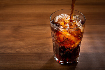 Coke glass with ice cubes on wooden table.