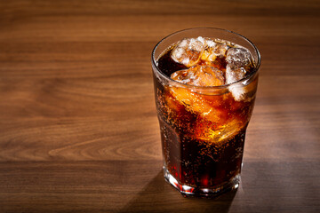 Coke glass with ice cubes on wooden table.