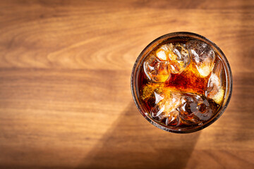 Coke glass with ice cubes on wooden table.