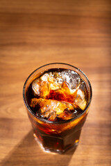 Coke glass with ice cubes on wooden table.