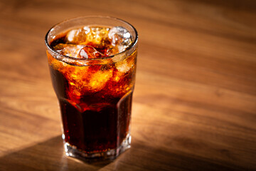 Coke glass with ice cubes on wooden table.