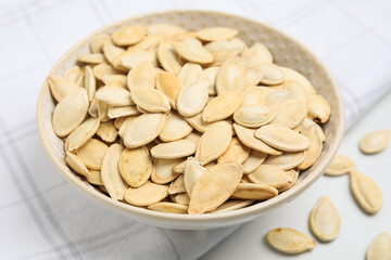 Bowl with pumpkin seeds on light table, closeup