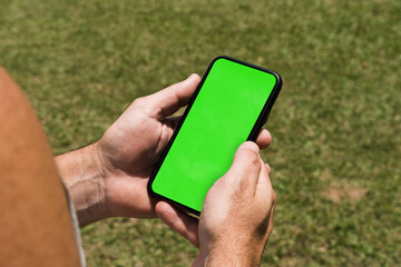 Man in the park holding a smartphone with green screen app on the screen. Rustic wooden table. Chroma Key