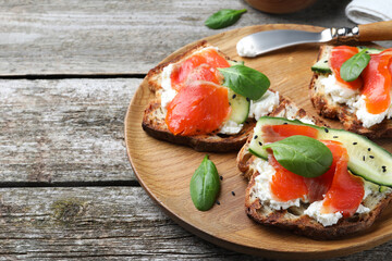 Delicious sandwiches with cream cheese, salmon, cucumber and spinach on wooden table. Space for text