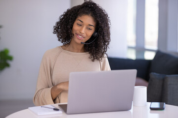 Young black woman at home remote working on laptop computer talking to her colleague