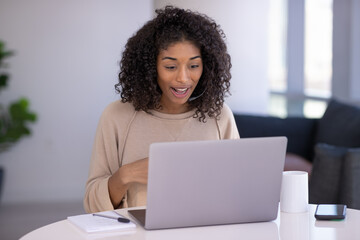 Young black woman at home remote working on laptop computer talking to her colleague