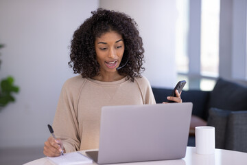 Young black woman at home remote working on laptop computer and smartphone