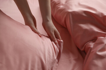 Woman making bed with beautiful pink silk linens, closeup view