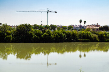 skyline with crane, palm trees and some houses on the leafy Guadalquivir river in Cordoba, Andalucia, Spain.