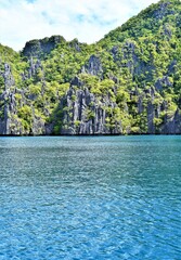 A limestone rock mountain is covered in mosses and shrubbery. The huge lime rock formation serves as a beautiful backdrop to the pristine lagoon