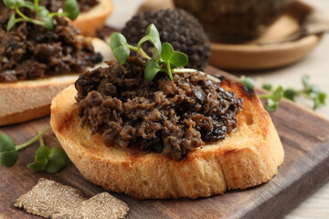 Delicious bruschetta with truffle sauce and microgreens on wooden board, closeup