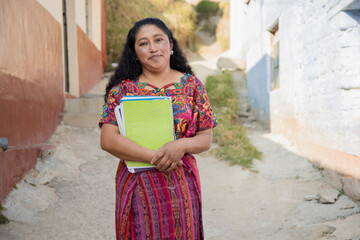 Hispanic mom with notebooks outside school in rural area - Mayan adult woman ready to go to study -...