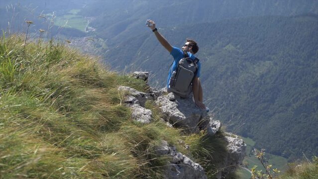 Active youg man takes selfie  on cliff above valley, bright sunny summer day