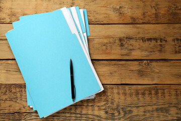 Turquoise files with documents and pen on wooden table, top view. Space for text
