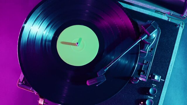 Vinyl record close-up. Vintage old vinil black phonograph spinning. Retro music player in pink purple neon light.