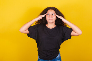 Brazilian, Latin American girl, for afro hair, yellow background, with hand on forehead and head,...