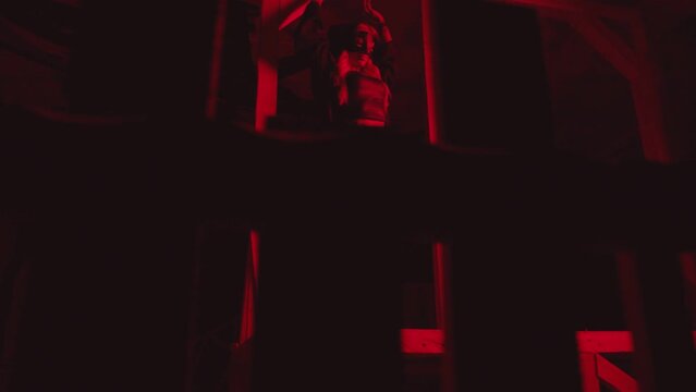 Young sexy woman in mask and black Halloween executioner costume dancing near old vintage wooden guillotine .  Girl with beautiful body with red hair wearing shorts dancing inside dark building . 
