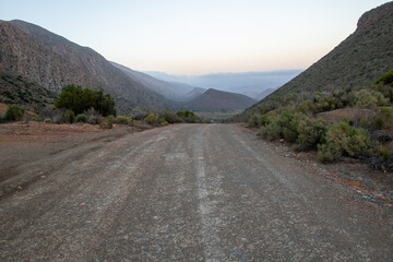 A gravel road leads down a valley with rolling hills in the Central Karoo region of South Africa