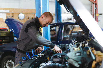 Fototapeta na wymiar Handsome mechanic in uniform is working in auto service garage. Repair service.