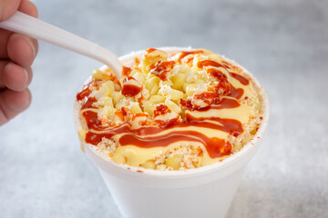 A view of a hand and spoon scooping a bite of esquites.