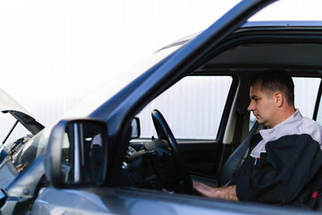 Fototapeta na wymiar Professional auto mechanic sitting in a car and using laptop to check car diagnostics.