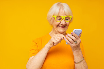 Photo of retired old lady talking on the phone in yellow glasses yellow background