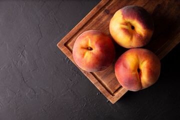Whole ripe peaches (Prunus persica) on rustic cutting board. Top view with copy space