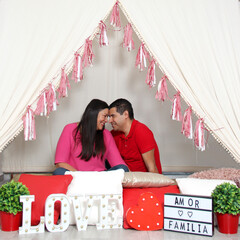 Latino adult couple shows their love under a teepee at a picnic to celebrate Valentine's Day of Love and Friendship in February as their anniversary with a sign that reads 