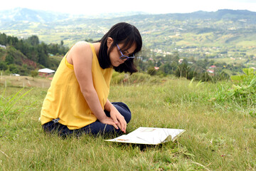 Beautiful girl with down syndrome, trisomy 21 reading a book outdoors.Peaceful landscape.