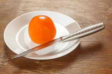 On a white plate lies an orange persimmon fruit with a knife.