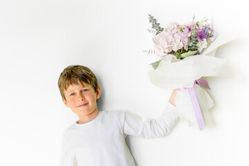 Charming boy holds a bouquet of flowers in his hand. Greeting card mockup with copy space. Portrait of a boy 8 years old, white, caucasian