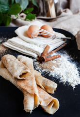 South African sweet cinnamon and sugar pancakes or “pannekoek" on black surface with selective focus and ingredients like eggs, flour and cinnamon in the background