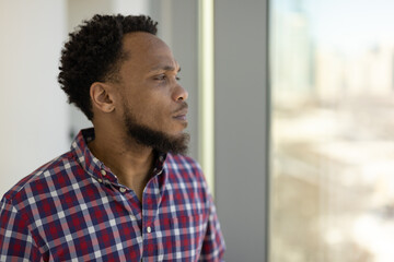 Black man feeling sad depressed face standing by a window looking outside
