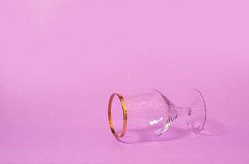 An empty wine glass lies on its side on a pink background