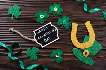 Handmade three-leaved shamrock horseshoe label and ivy hat on wooden background flat view