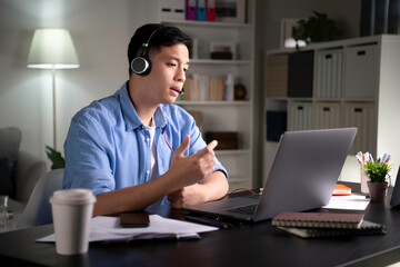 Focused young Asian business person, entrepreneur, speaker, student, office worker wearing headphones, looking at laptop screen and speaking in video conference call, giving lecture, joining online 