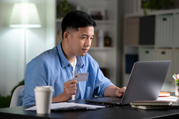 Confident young Asian man, online customer doing online shopping, browsing shop websites, making online payment transaction using laptop and holding credit card at home.