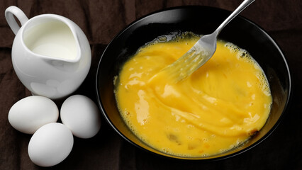Scrambled eggs, omelette. Сhef whisking eggs in black bowl cooking omelette with milk. Traditional heathy breakfast