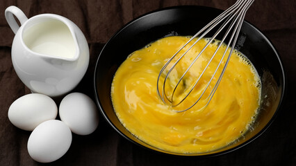 Scrambled eggs, omelette. Сhef whisking eggs in black bowl cooking omelette with milk. Traditional heathy breakfast