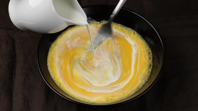 Chef pouring milk and mixing eggs with whisk. Cooking Scrambled eggs, omelette