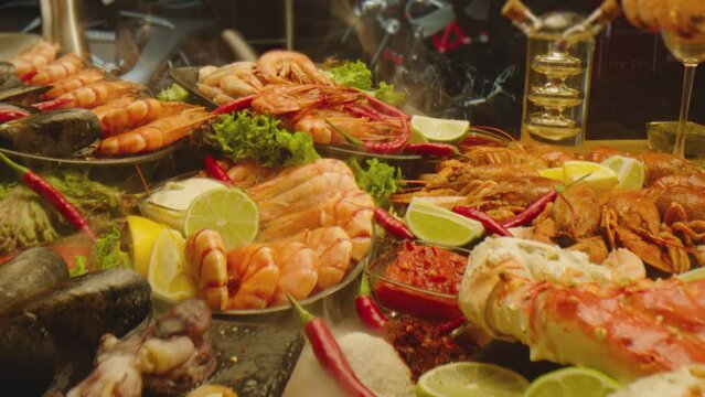 Beautiful delicious composition of prepared table in restaurant . Tasty seafood with hot sauces . Set of mussels , crayfishes , lobster , various shrimps . Camera moving trough table for beer party