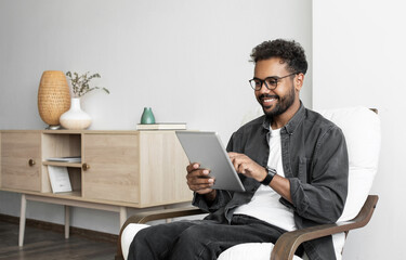 Young smiling man using digital tablet computer at home, Leisure, relaxation, online learning, web chat, video call, freelance, modern lifestyle concept.